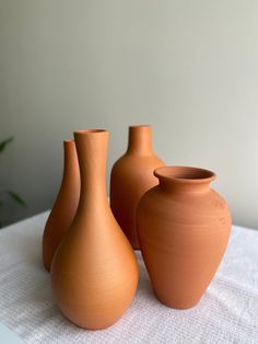 three brown vases sitting on top of a white table cloth covered table with a plant in the background