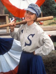 a woman holding a baseball bat in front of an american flag and another person behind her