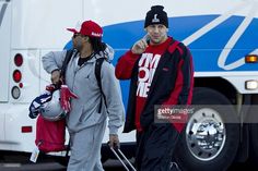 two men walking down the street with their luggage and one man pointing at his camera