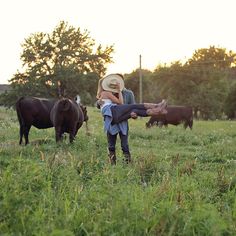 two people standing in a field with cows behind them and one person holding the other