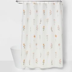 a white shower curtain with pink and yellow flowers on it next to a bathtub