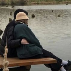 two people are sitting on a bench by the water with ducks in the background,