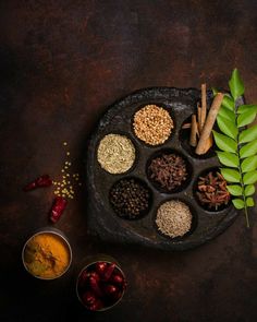 an assortment of spices and herbs arranged in a black tray on a dark background with leaves