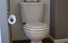 a white toilet sitting inside of a bathroom next to a wall mounted paper dispenser