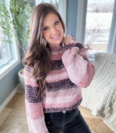 a woman is standing in front of a window wearing a pink and black striped sweater