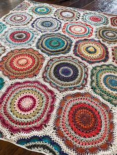 a multicolored crocheted afghan on a wooden floor in front of a fireplace