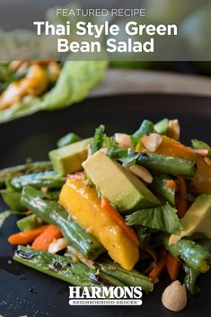 a black plate topped with green beans, carrots and avocado next to lettuce