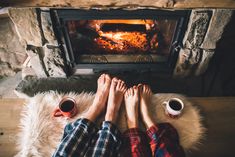 two people sitting in front of a fireplace with their feet up on the floor next to each other