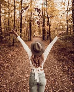 a woman with her arms wide open in the woods, wearing jeans and a hat