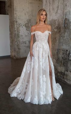 a woman in a white wedding dress standing next to a concrete wall and posing for the camera