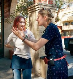 two young women standing next to each other on a city street, one holding her hand out