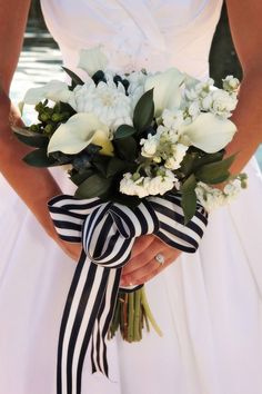 a woman in a white dress holding a bridal bouquet with black and white ribbons