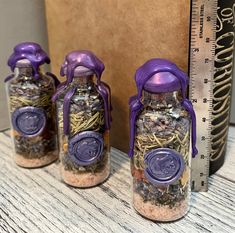 three glass jars with purple decorations on them next to a measuring tape and bookcase