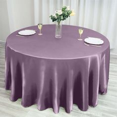 a round table covered in purple satin with white plates and silverware on the table