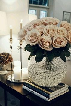 a vase filled with pink roses sitting on top of a table next to two candles