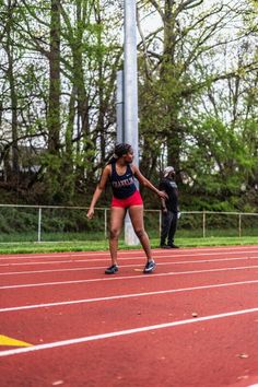 a woman running on a race track with another person behind her watching from the sidelines