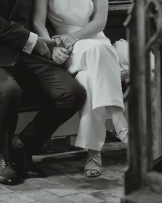 a man and woman sitting next to each other on top of a wooden bench in black and white