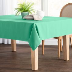 a green table cloth on top of a wooden table with two chairs and a potted plant