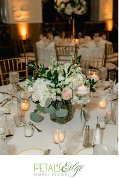 the centerpieces on this table are filled with white flowers and greenery as well as candles