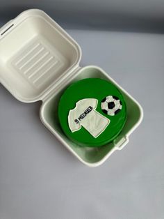 a plastic container with a cake in the shape of a shirt and soccer ball on it