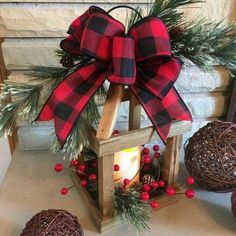 a lantern with a red and black plaid bow on it next to some pine cones