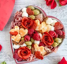 a heart shaped bowl filled with assorted fruits and nuts