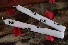 two white candles sitting on top of a wooden table next to red flowers and petals