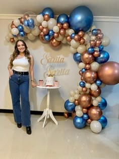 a woman standing next to a table with a cake on it and balloons in the background