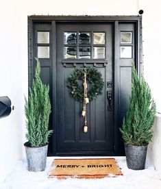 two potted plants are next to a black door with a wreath on the front