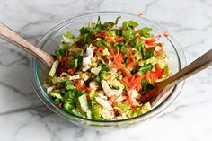 a salad in a glass bowl with wooden spoons on a marble countertop, ready to be eaten