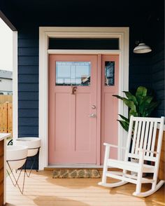 a white rocking chair sitting on top of a wooden porch next to a pink door