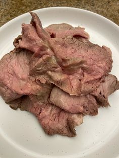 a white plate topped with sliced meat on top of a table