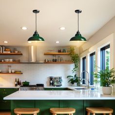 a kitchen with green cabinets and stools in front of the counter top, along with two hanging lights over the sink