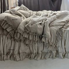 an unmade bed with ruffled linens in front of a curtained window