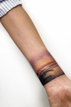 a man's arm with a palm tree and sunset tattoo on the left wrist