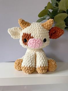 a crocheted cow sitting on top of a white shelf next to a potted plant