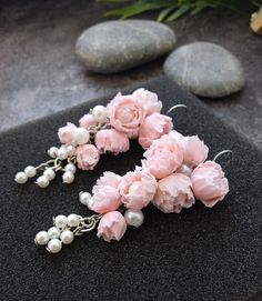 pink flowers and pearls hang from silver earwires on a black surface next to some rocks