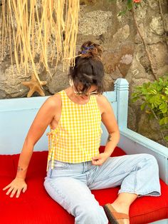 a woman sitting on top of a red cushion next to a stone wall and plants