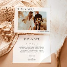 two wedding thank cards sitting on top of a bed next to a white feather fan