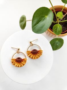 a pair of sunflower earrings sitting on top of a white table next to a potted plant