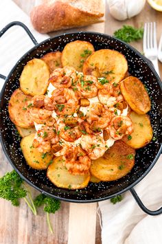 shrimp and potatoes in a skillet with parsley on the side next to bread