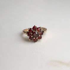 A Vintage 9 carat gold Garnet cluster ring. This beautiful piece holds a gorgeous collection of deep red stones in a gold setting, holding them high up on display. CONDITION: Wear consistent with age and use. Please see photos for more detail. HALLMARKED 9 CARAT GOLD, ASSAYED PRE 1975 STONE SIZE: 5mm (.50 carat) 3mm (.10 carat) SETTING DIAMETER: 12mm SETTING HEIGHT: 7mm BAND WIDTH: 1.5mm RING SIZE: UK: M | US: 6 1/4 WEIGHT: 3.0 grams (UZZ) Yellow Gold Garnet Cluster Ring As Gift, Gold Garnet Cluster Promise Ring, Heirloom Garnet Cluster Ring With Gemstones, Heirloom Garnet Cluster Ring For Anniversary, Heirloom Style Round Garnet Cluster Ring, Heirloom Style Garnet Cluster Ring, Heirloom Garnet Cluster Ring, Heirloom Style Red Garnet Cluster Ring, Heirloom Red Garnet Cluster Ring