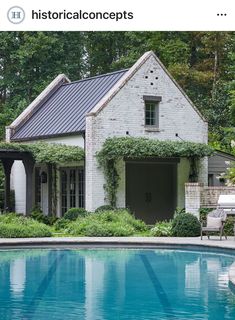 the pool is surrounded by greenery and an old brick house with a metal roof