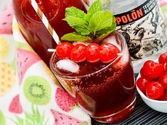 two glasses filled with liquid and berries next to a bowl of cherries on a table