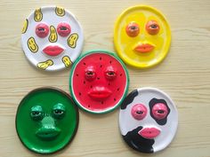 four plates with faces painted on them sitting on a wooden table next to each other