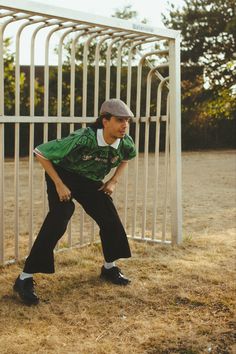 a man leaning against a metal fence in front of a white gate with his hands on his hips