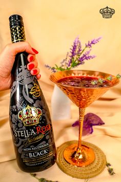 a woman holding a bottle of wine next to a glass filled with liquid and garnished with flowers