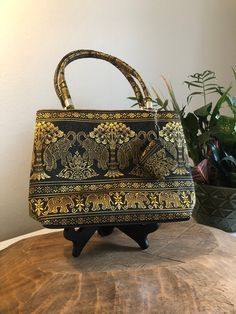 "This bag looks like it is from India but it could be from Singapore as well. It looks well made and has embroidered, ornate elephants and other designs. The tiny coin purse is also attached. It looks like it was never used. No damage or marks on it. We disclose as much as we know about an item. Our items are vintage, gently used pieces, (with the exception of a few handmade products.) They may have flaws or wear. Check out the pictures to ensure you know what you are buying. All products are \" Traditional Gold Shoulder Bag For Travel, Traditional Gold Shoulder Bag For Daily Use, Gold Embroidered Tote Bag, Black Rectangular Shoulder Bag For Festivals, Gold Rectangular Coin Purse For Daily Use, Rectangular Gold Coin Purse For Daily Use, Gold Handheld Shoulder Bag Gift, Vintage Gold Bag For Festivals, Vintage Gold Bags For Festivals