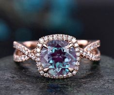 an engagement ring with a purple diamond surrounded by white and rose gold band, on top of a rock