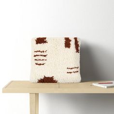 a white and brown rug sitting on top of a wooden shelf next to a book